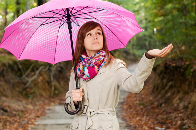 人行道带着雨伞的漂亮女孩在检查雨水围巾鲜艳的颜色森林