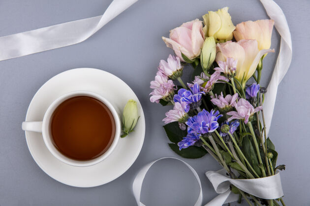 灰在灰色背景下 白色丝带和一杯茶的鲜花俯视图茶花丝带