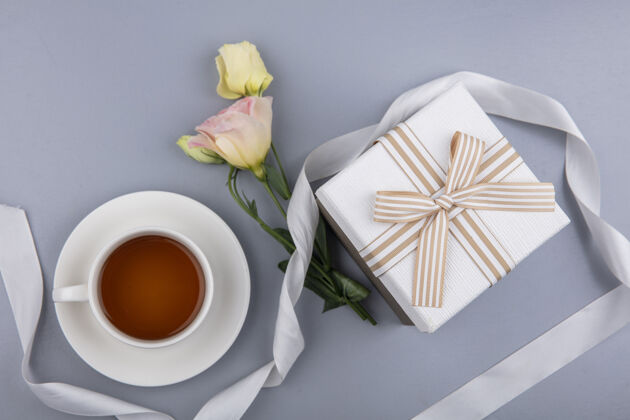 顶部白色礼盒彩带和灰色背景上的一杯茶的可爱花朵俯视图盒子白灰