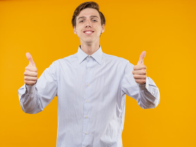 年轻身穿白衬衫的年轻人站在橙色的墙上 微笑着自信地竖起大拇指站立男人展示