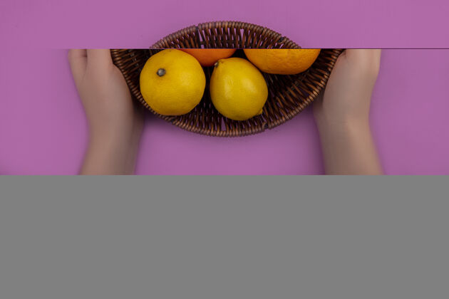 柑橘俯视图：一个粉红色背景的篮子里 一个女人手里拿着葡萄柚 柠檬和橘子保持葡萄柚视野
