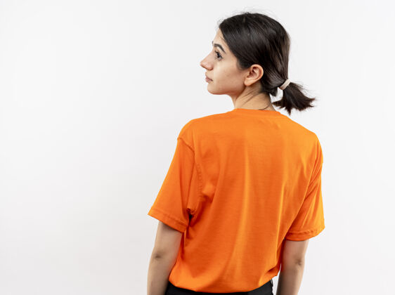 女孩穿着橙色t恤的年轻女孩站着 背对着白色的墙壁年轻橙色背