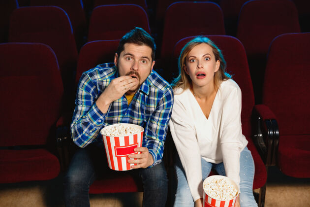 娱乐迷人的年轻白种人夫妇在电影院 房子或电影院看电影看起来富于表现力 惊讶和情绪化独自坐着玩关系 爱情 家庭 周末时间生活方式划船表达