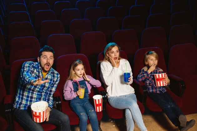吃年轻的白种人家庭在电影院 房子或电影院看电影看起来富有表现力 惊讶和情绪化独自坐着玩关系 爱情 家庭 童年 周末时间看女看