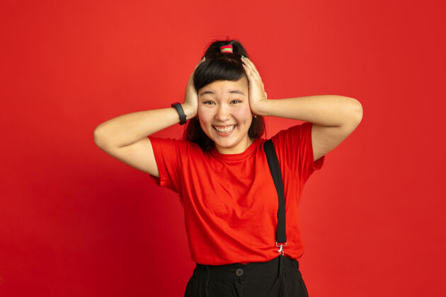 人类亚洲青少年的肖像画被隔离在红色工作室的背景上美丽的深色头发的女性模特 随意的长发人类情感的概念 面部表情 销售 广告惊讶 震惊手势青少年专业