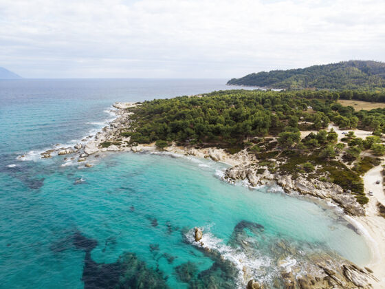 海湾爱琴海沿岸有蓝色透明的海水 周围绿树成荫 岩石 灌木丛和树木 从无人机希腊俯瞰度假村海滩爱琴海