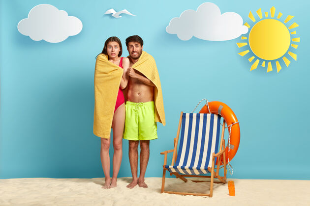 海滩困惑的女人和男人在毛巾下发抖 觉得冷 游泳后试着暖和比基尼休闲毛巾