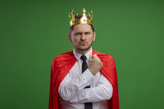 超级英雄穿红斗篷的超级英雄商人戴着王冠 严肃的脸站在绿色的墙上不高兴站商人看