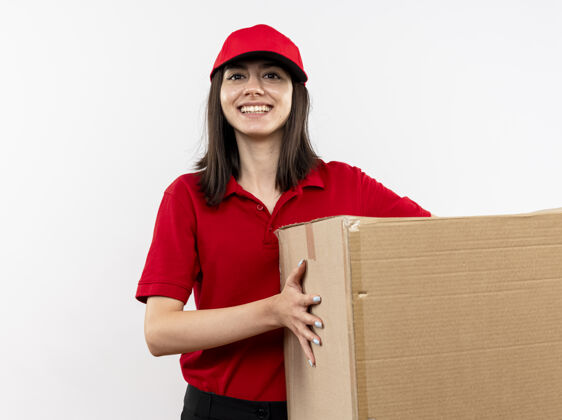 站着年轻的送货员身穿红色制服 戴着帽子 手里拿着大纸盒 脸上带着微笑站在白色的墙上盒子帽子女孩