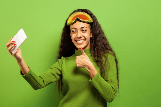 表情以绿色工作室为背景 黑色皮肤的非洲裔美国年轻女子滑雪面具肖像关于人类情感 面部表情 销售 广告 冬季运动和假期的概念自拍或虚拟博客运动女性黑发
