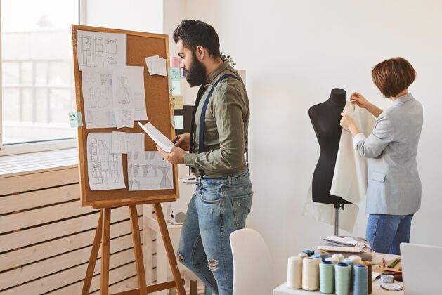 男性侧视图时装设计师在工作室与服装形式和想法板男性线工作室