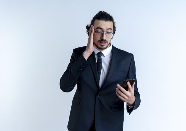 优雅一个穿着黑西装戴着眼镜的商人站在白墙上看着智能手机的屏幕 困惑而焦急焦虑人眼镜