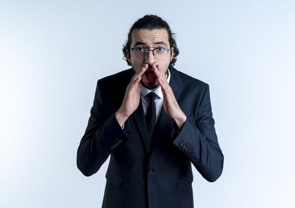 男人穿黑西装戴眼镜的商人站在白墙上 手靠嘴边喊或叫摆姿势人生意