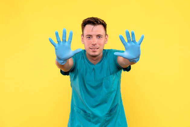 青年黄墙上戴着蓝手套的男医生的正视图手医疗男人