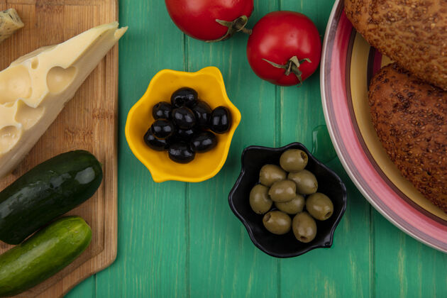 柔软黑色和绿色的橄榄在一个碗上 黄瓜和奶酪放在一个木制的厨房板上 软芝麻饼放在一个绿色的木制背景板上新鲜奶酪黑色