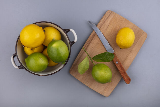 食品在灰色背景下 用刀架在砧板上的平底锅里 俯瞰柠檬和酸橙顶部切割灰色