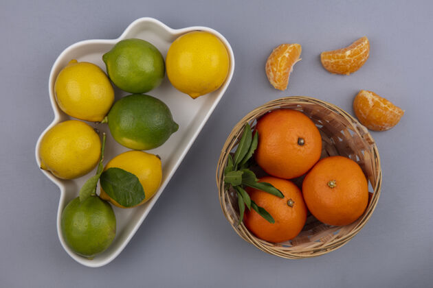 酸橙在灰色的背景下 用云彩形状的盘子和篮子里的橙子顶上看柠檬橘子顶部篮子