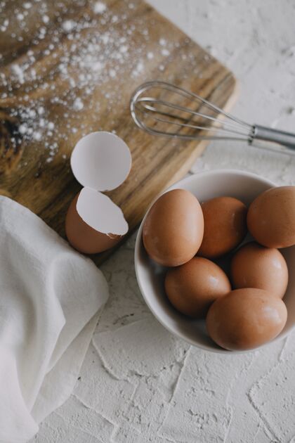 搅拌垂直拍摄一碗鸡蛋和一个银色的搅拌器旁边的一个白色表面上的砧板搅拌器板金属