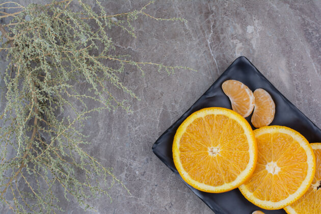 新鲜橘子和橘子片放在黑盘子里柑橘克莱门汀美味