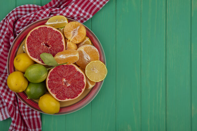 空间俯视复制空间切半葡萄柚与去皮的橙子和柠檬与石灰在一个盘子上的红色格子毛巾绿色背景盘子毛巾视图
