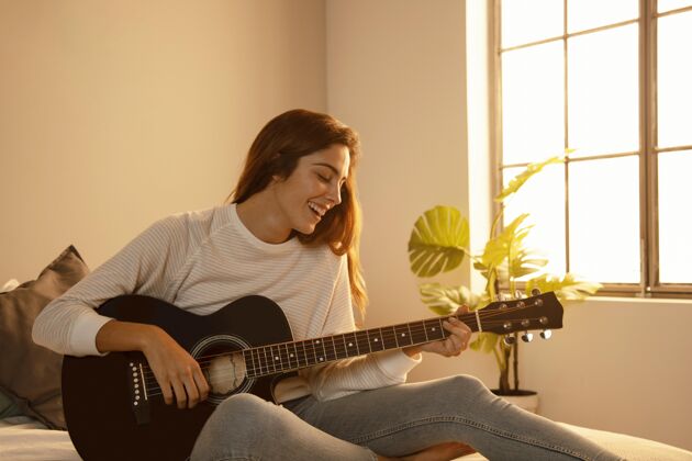 室内笑脸女人在家里弹吉他在床上吉他假期逗留
