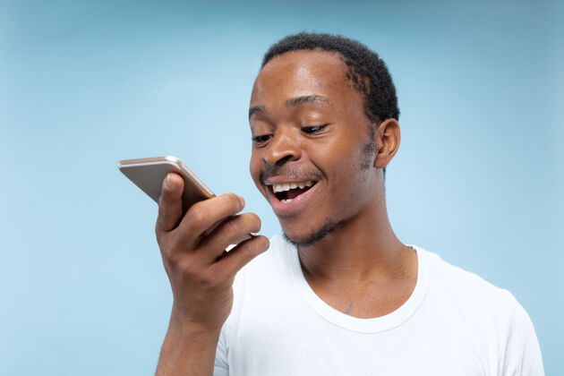 职业身穿白衬衫 蓝色背景的非洲裔美国青年半身像人类情感 面部表情 广告 销售理念手持智能手机 交谈或录制语音信息表情高管长相