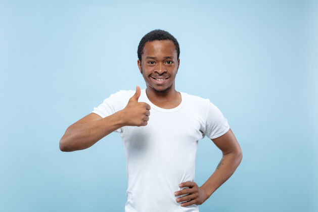 衬衫在蓝色工作室背景上 年轻的非洲裔美国男模身穿白衬衫的半身特写肖像人类情感 面部表情 广告概念显示ok的标志很好可以男性工作