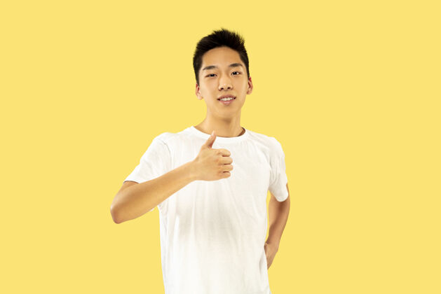 手势黄色工作室背景上的韩国年轻人半身像穿着白衬衫的男模微笑着 露出ok的标志人类情感的概念 面部表情微笑韩国人表情