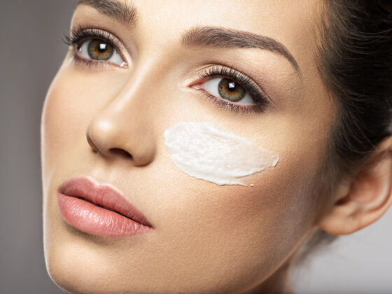 化妆品年轻漂亮的女人用化妆霜涂抹在脸上靠近眼睛的地方护肤理念美容理念女人美容眼部