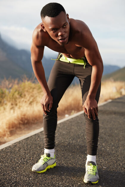 公路运动和决心的概念深色皮肤 运动型身材的家伙的垂直镜头在环山公路上跑步 享受乡村新鲜空气 在户外做积极的锻炼 穿着运动鞋运动山地教练