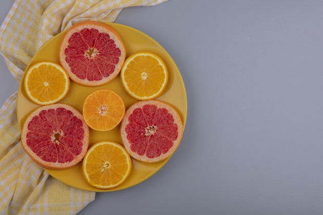 顶部顶视图复制空间葡萄柚片与橙色片在一个黄色的盘子与黄色格子毛巾在灰色的背景灰色柑橘复制