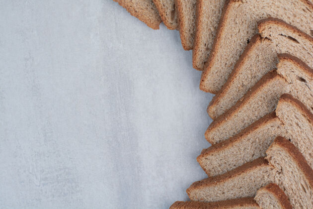 烘焙大理石背景上的新鲜棕色面包片糕点棕色小吃