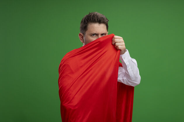 包装超级英雄商人裹着红色斗篷 严肃的脸站在绿色的背景下看着相机超级商人脸