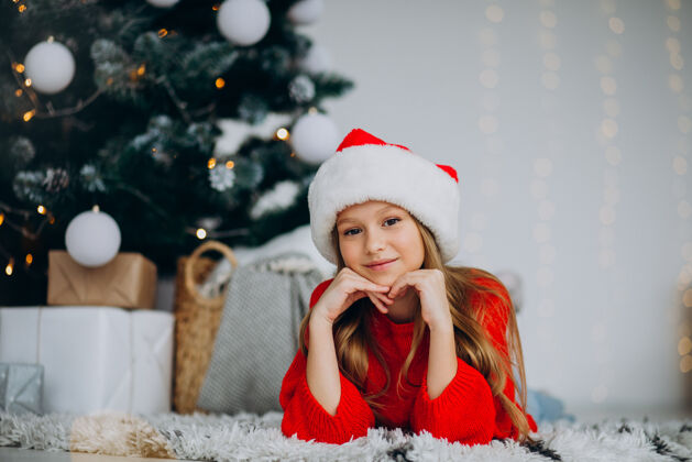 节日圣诞树下戴圣诞帽的漂亮女孩年轻灯欢呼