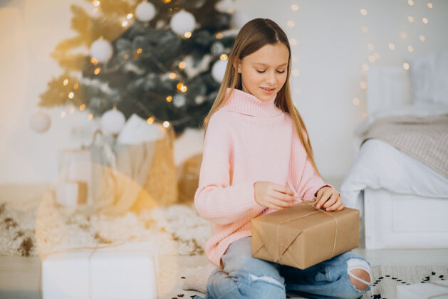 光明可爱的女孩拿着圣诞礼物在圣诞树旁看举行人