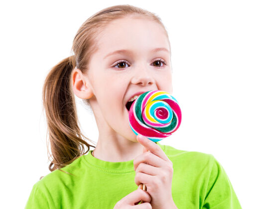 积极微笑的小女孩穿着绿色t恤 吃着彩色的糖果-白色的隔离小孩子表情