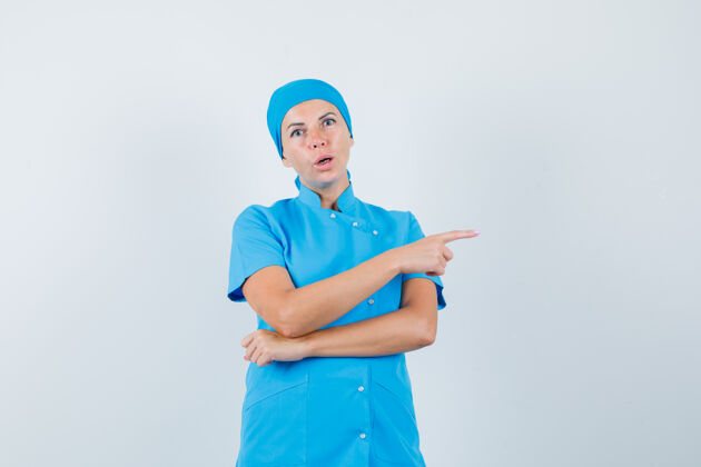 年轻人穿着蓝色制服的女医生指着侧面 惊讶地看着 正前方指点制服诊所