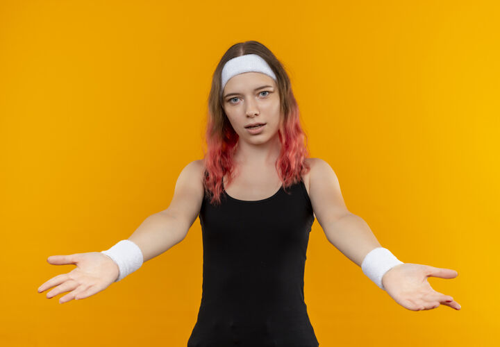 运动身着运动服的年轻健身女士站在橙色的墙上做欢迎手势运动市民年轻