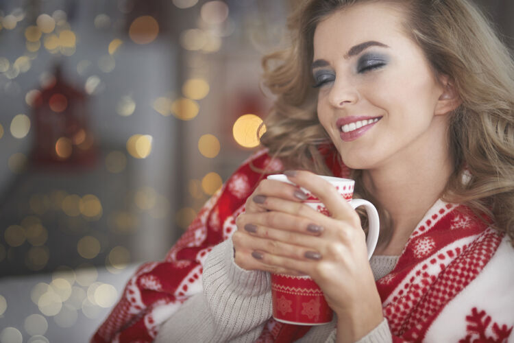 放松年轻的金发女人在喝热巧克力闭上眼睛庆祝杯子
