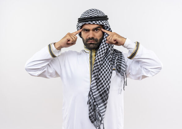 阿拉伯语身着传统服装的阿拉伯男子站在白墙上 用严肃自信的表情指着他的太阳穴男人指向表情