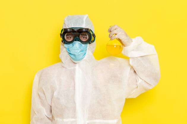 烧瓶正面图穿着特殊防护服的男科学工作者拿着黄色表面有黄色溶液的烧瓶化学科学套装