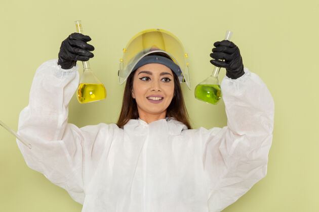 防护正面图穿着特殊防护服的女化学家在绿色表面上用不同的溶液工作套装女工作