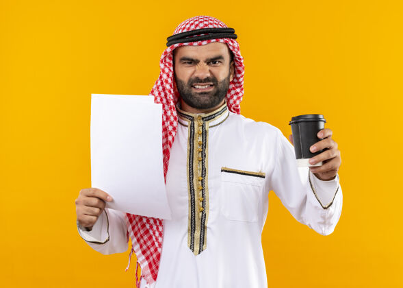 传统身着传统服饰的阿拉伯商人手持文件和咖啡杯 愤怒的脸站在橙色的墙上阿拉伯语愤怒脸