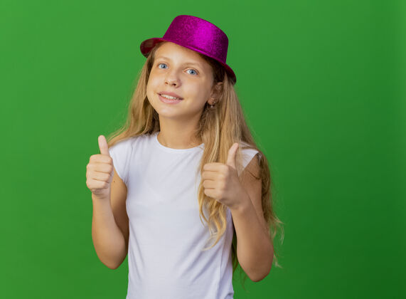 向上戴着节日帽子的漂亮小女孩微笑着竖起大拇指帽子秀节日