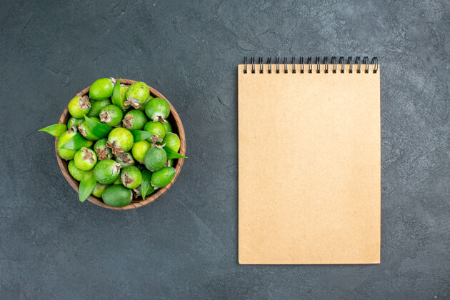 可食用的坚果在黑暗的表面上用桶记事本俯视新鲜的feijoas豌豆顶部菜