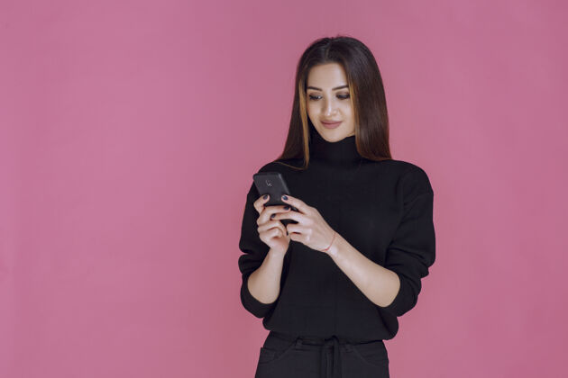 聊天穿着黑色毛衣的女人拿着智能手机发短信或查看社交媒体设备智能个人