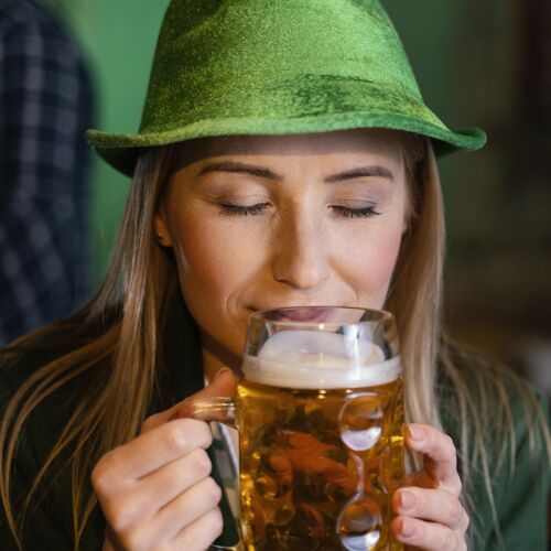 品脱戴着帽子的女人的正面图 用饮料庆祝圣帕特里克节活动爱尔兰三叶草