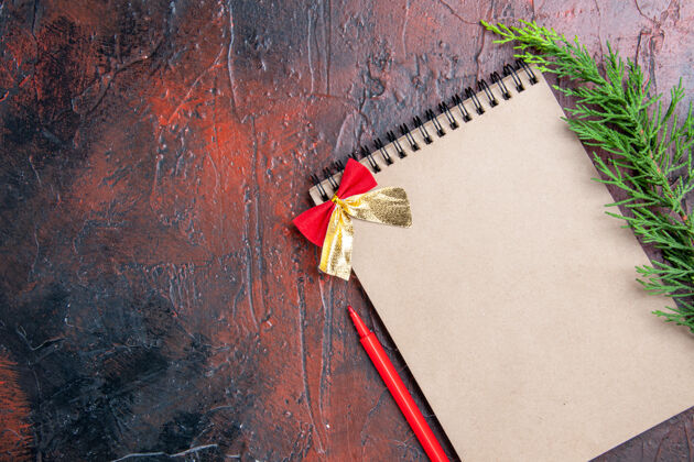 松树顶视图红色笔一个小蝴蝶结的记事本一个松树枝在暗红色的表面与复制空间的权利钢笔书签装订