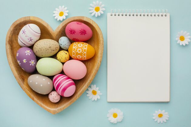 纪念彩色复活节彩蛋在心形板与笔记本和鲜花俯视图心花静物