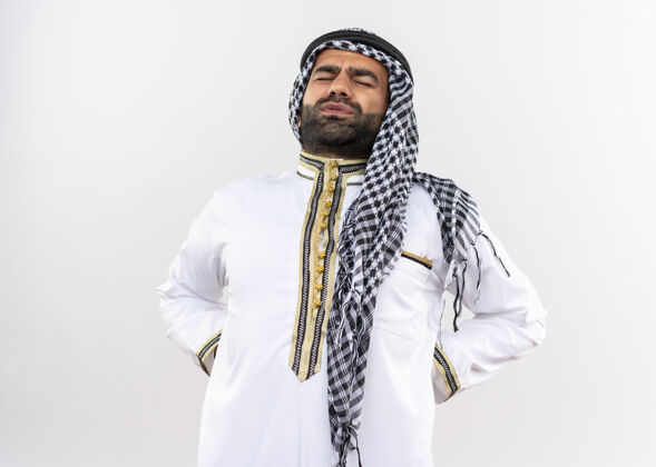 摸阿拉伯男人穿着传统的衣服 站在白墙上摸背 看起来很不舒服男人不舒服疼痛